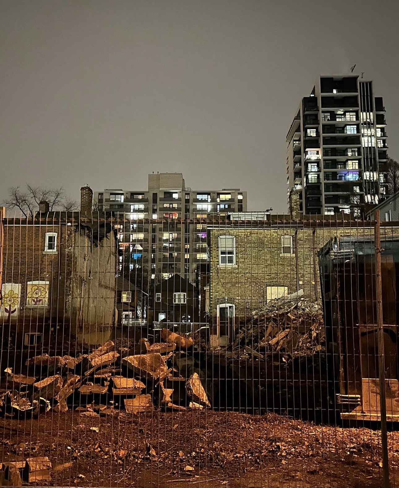 Demolition rubble and remaining brick wall at night with condo towers behind